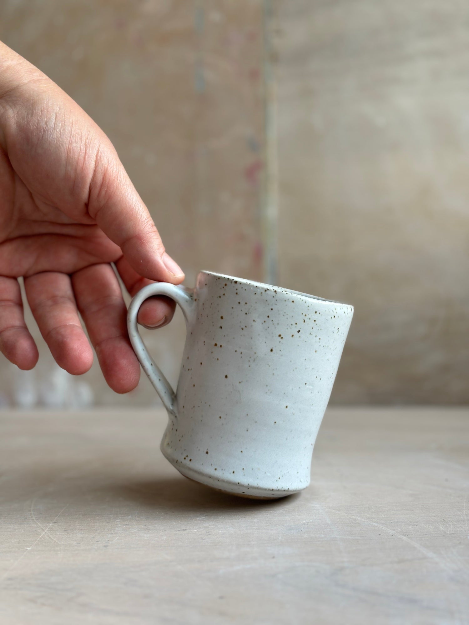 A hand holding a white speckled mug.