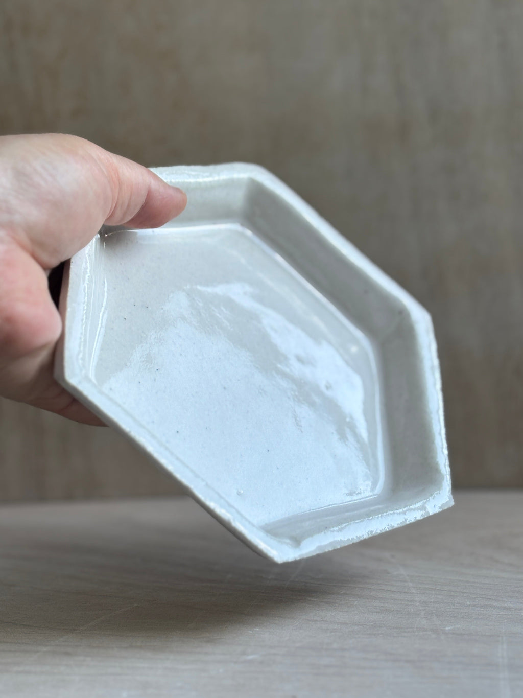 Hexagonal white ceramic dish held by a hand on a wooden surface